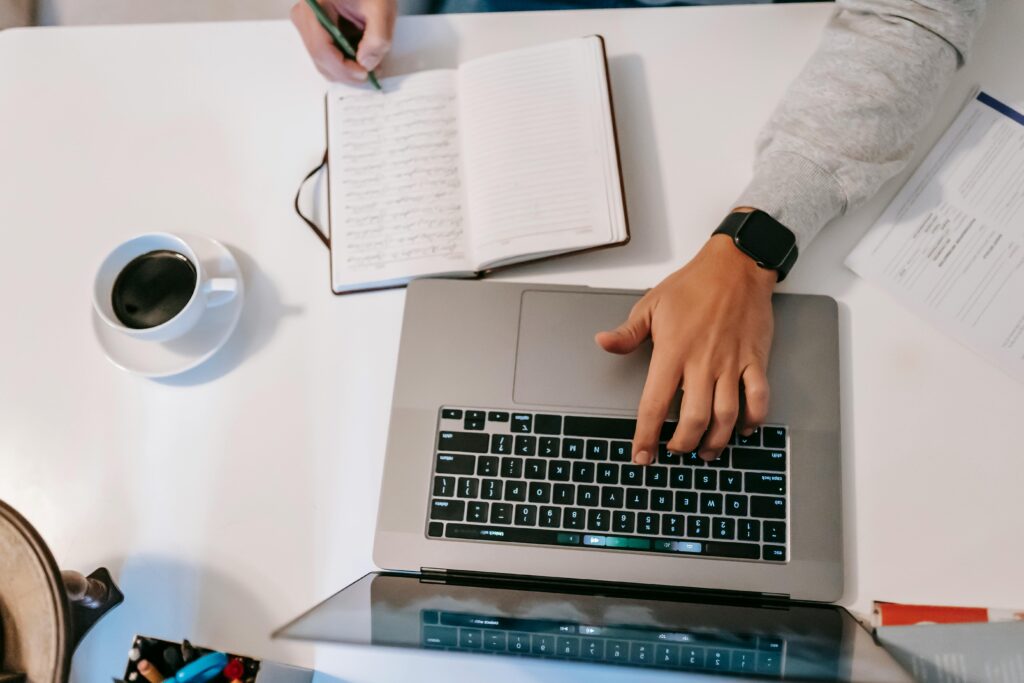 A top-down view of a home office setup with a laptop, notebook, and coffee.